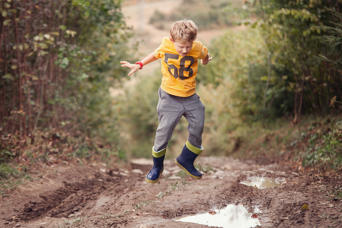 Boy puddle jumping in the woods