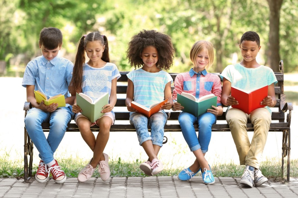 Five kids reading on a bench outside