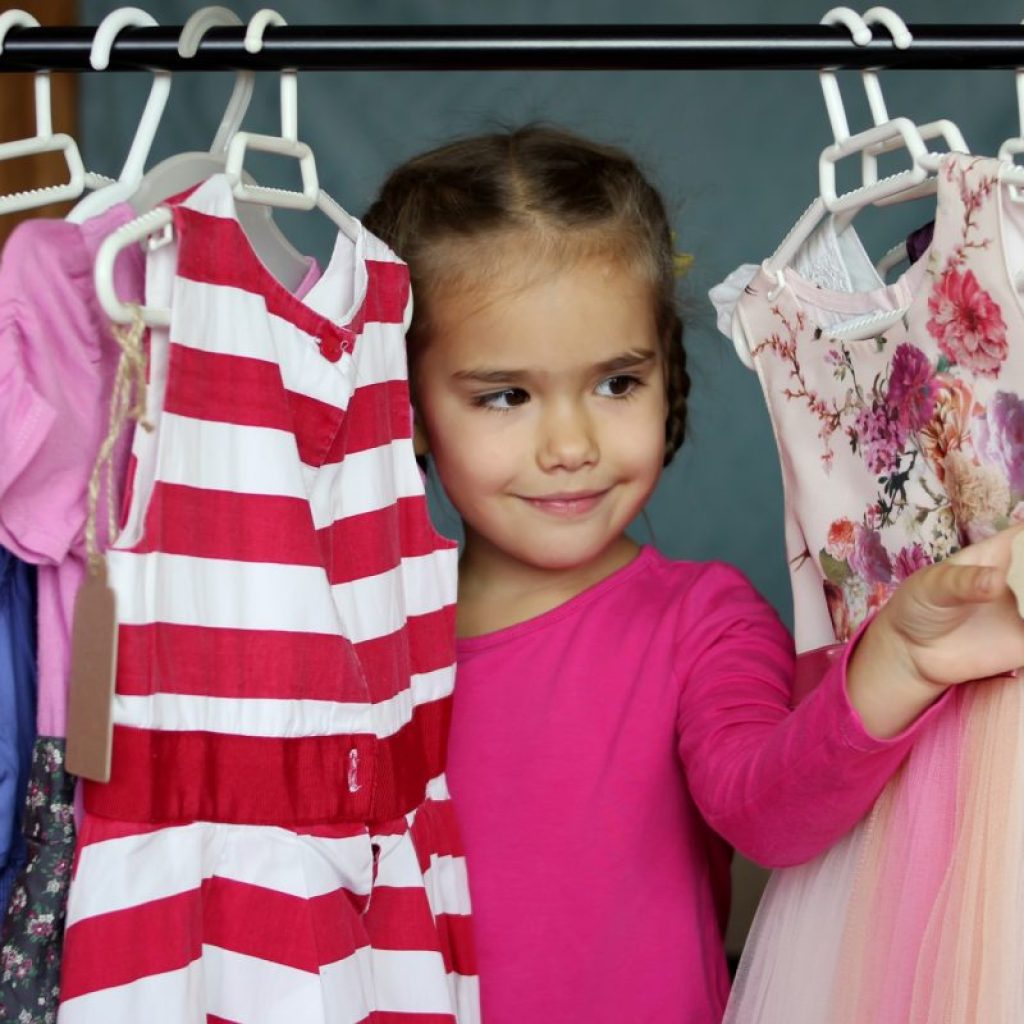 Little girl peering through clothes hanging in closet.