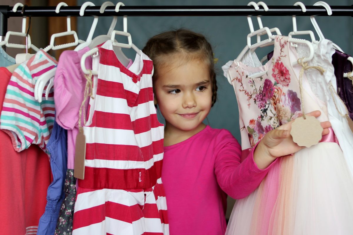 Little girl peering through clothes hanging in closet.
