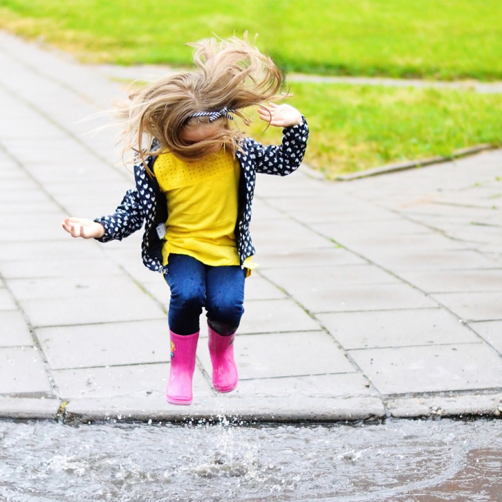 Little girl with rubber boots jumping in a puddle