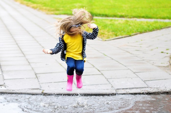 Little girl with rubber boots jumping in a puddle