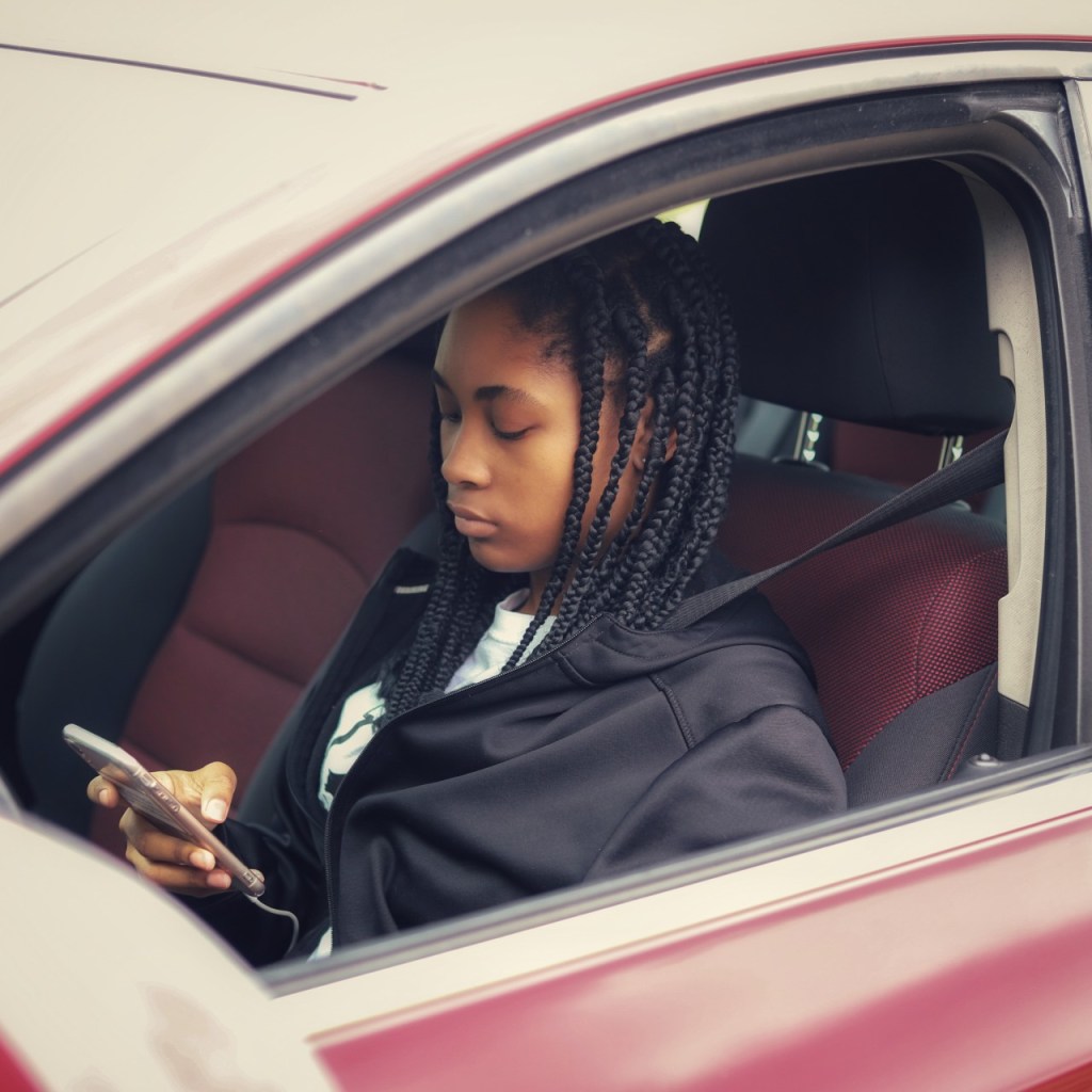 Teen on her phone in the drivers seat of a car