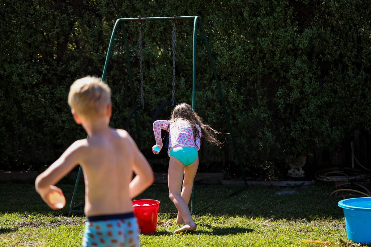 Kids throwing water balloons at each other in the backyard