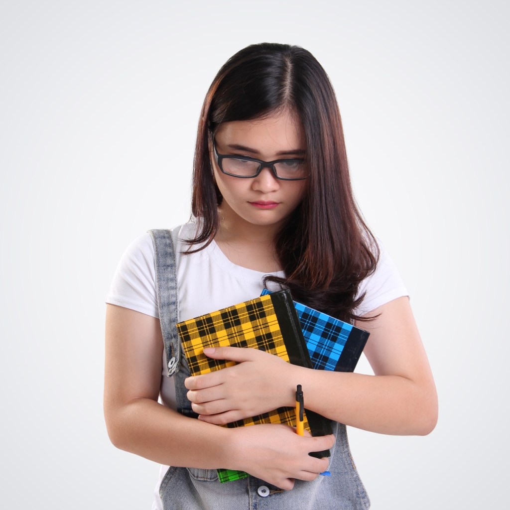 An awkward teenager holding her books with her head bent down