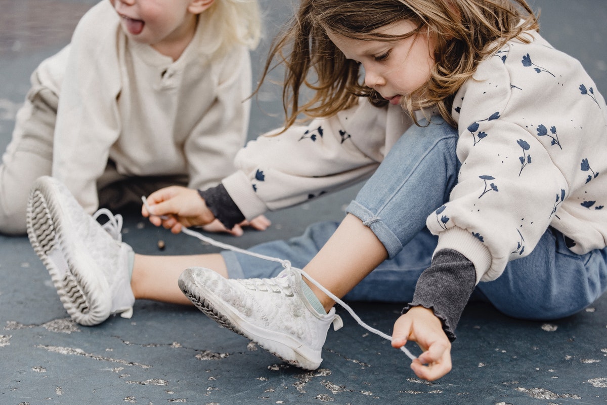 girl showing a friend how to tie her shoes