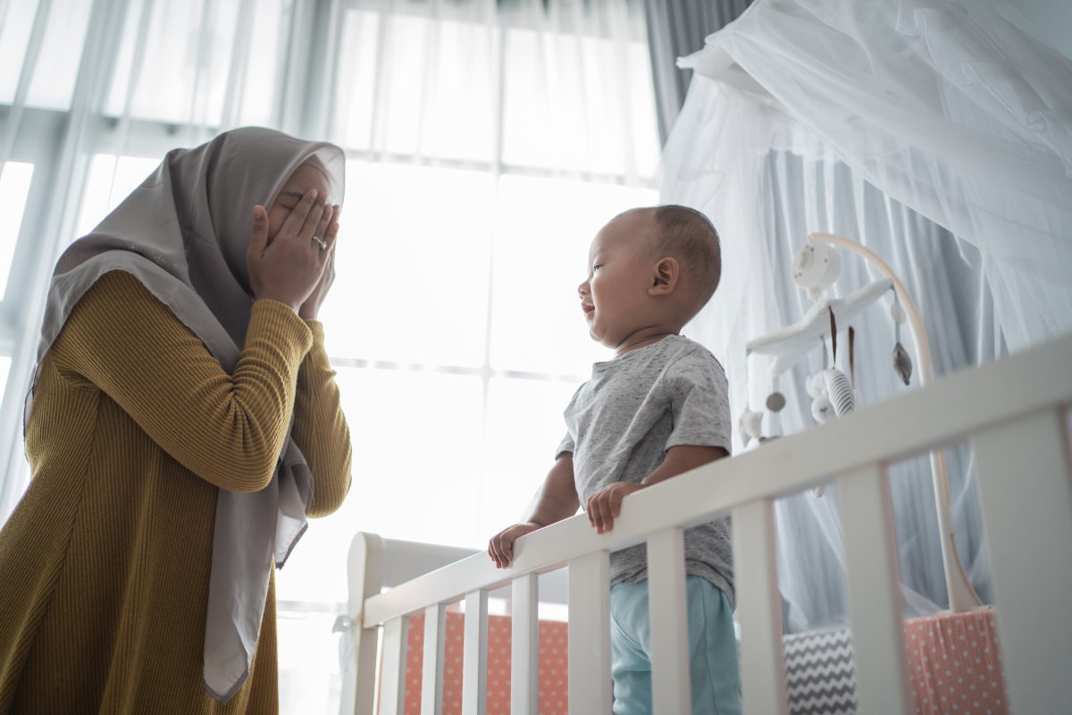 Mom playing peekaboo with son in crib.