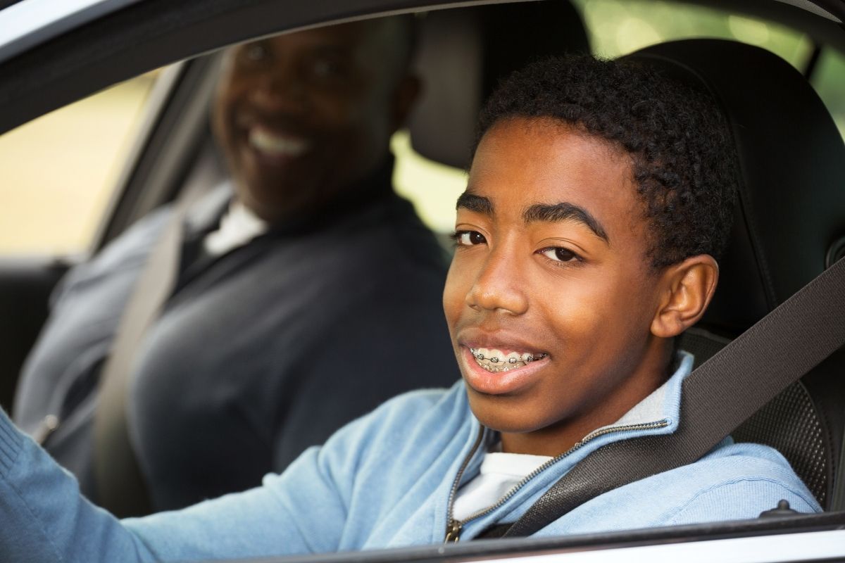 A teen boy at the wheel with parent watching