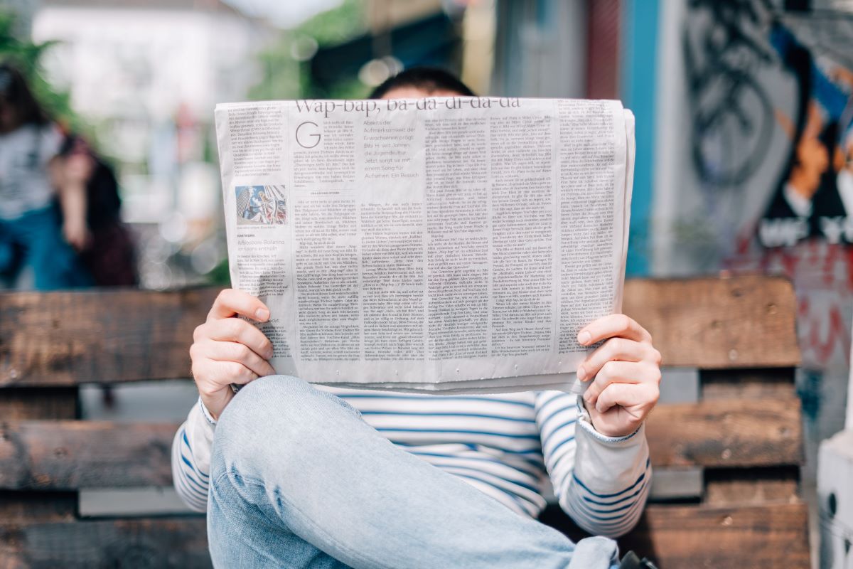 man reading a newspaper sitting on a bench