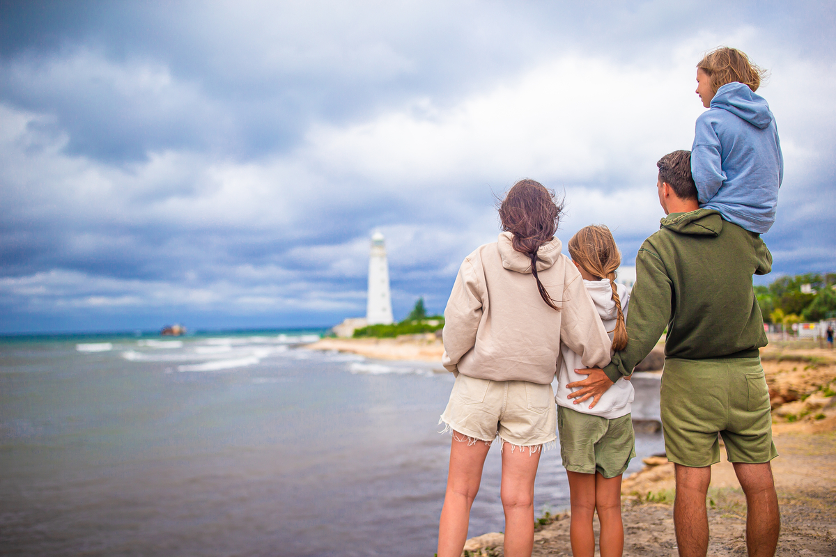 A family standing on the shoreline with a lighthouse in the background.
