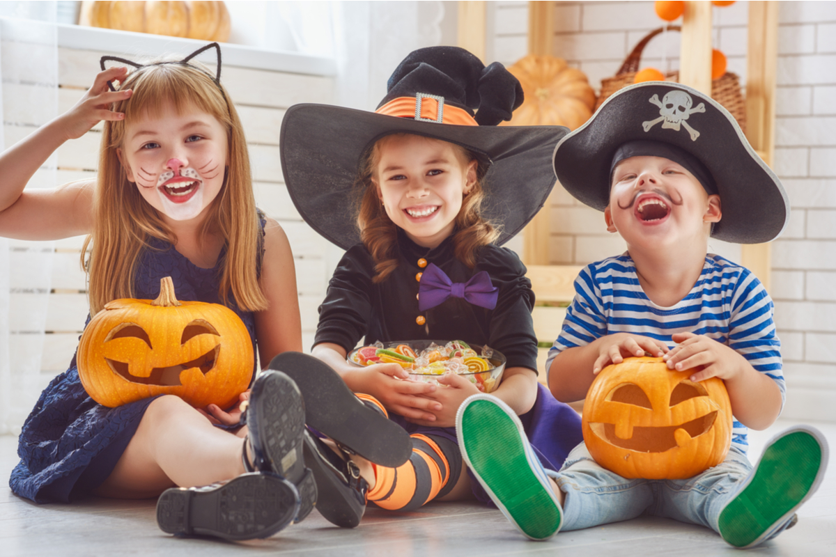 A group of children sitting with Halloween costumes on holding pumpkins.