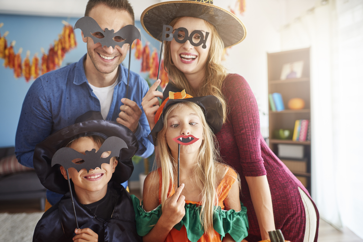 A family taking a cute picture holding Halloween props over their faces.