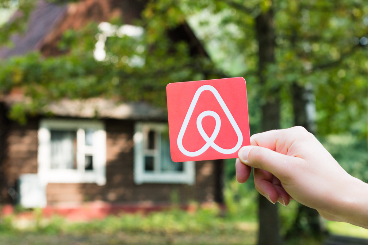 A hand holding an Airbnb sign with a cabin in the background.