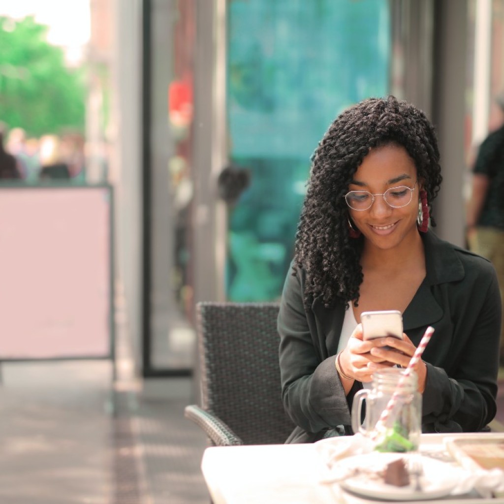 woman looking at her phone while sitting at an outdoor cafe