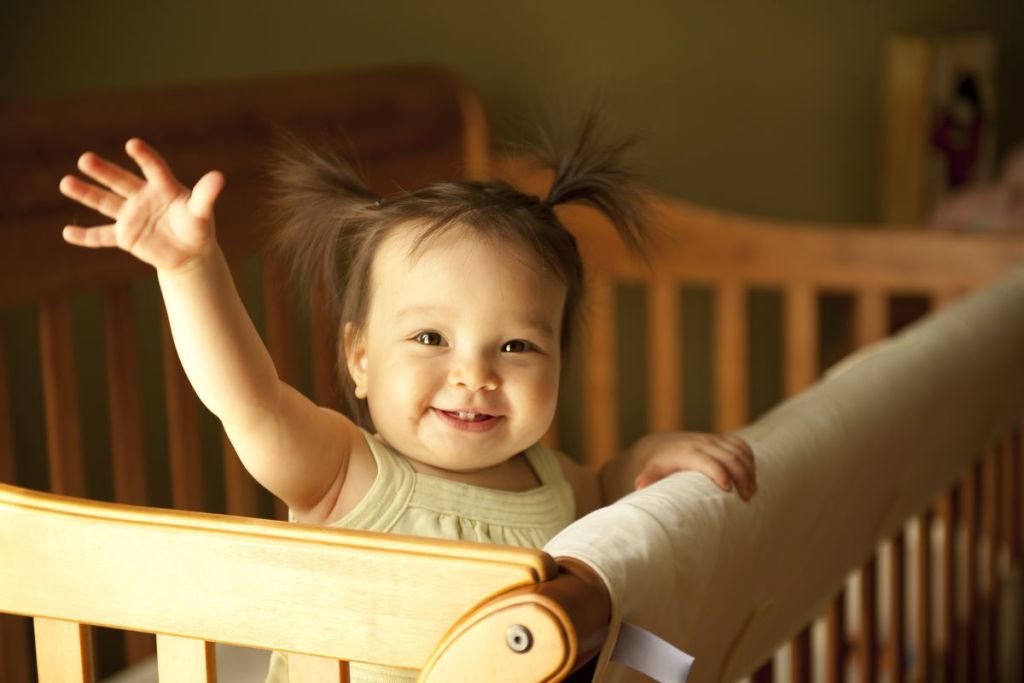 Baby girl standing and waving in crib