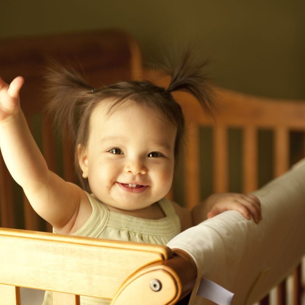 Baby girl standing and waving in crib.