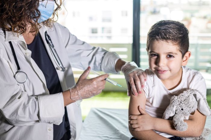 Little boy getting a vaccine from the doctor while holding a stuffed animal