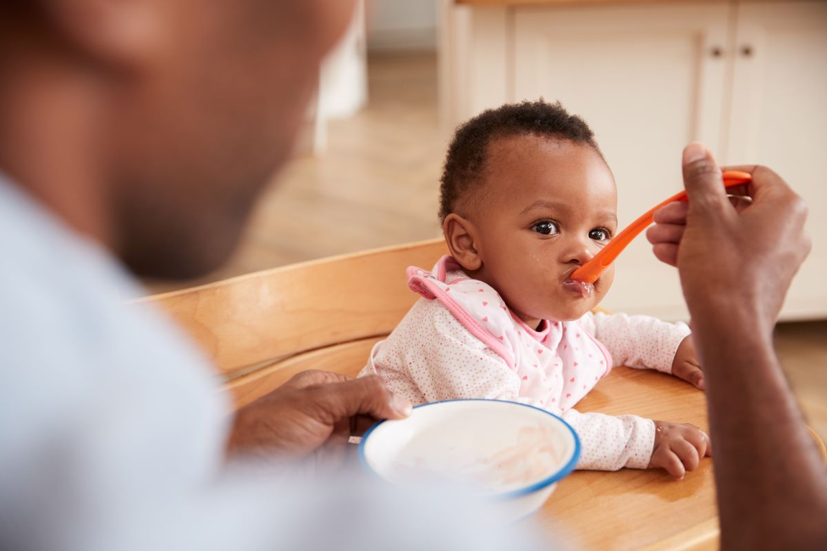 Dad spoon feeds baby in highchair.