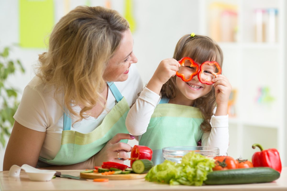 A mother and daughter cooking in the kitchen, with the child holding pepper slices up to her eyes