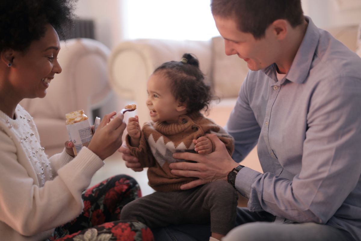 Dad holding daughter on lap while Mom feeds her