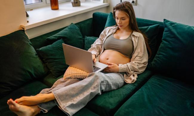Pregnant woman relaxing on a couch with her laptop