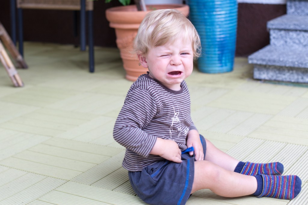 A toddler boy sitting down throwing a tantrum.
