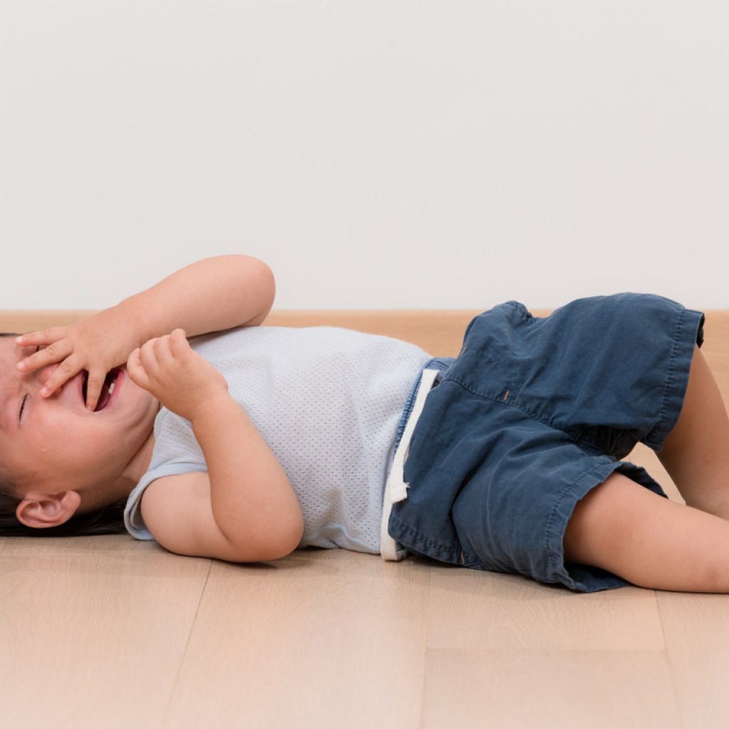 A toddler boy throwing a tantrum on the floor.