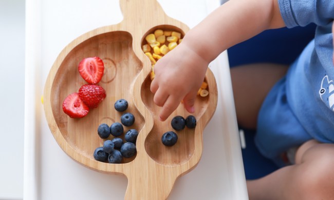 A toddler grabbing some food off of a plate.