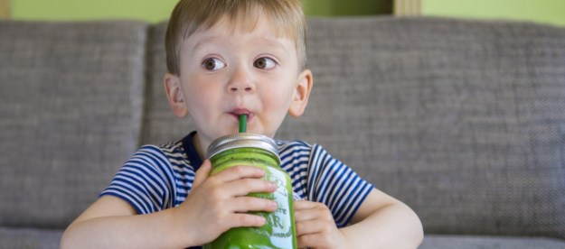 A little boy drinking a green smoothie drink.