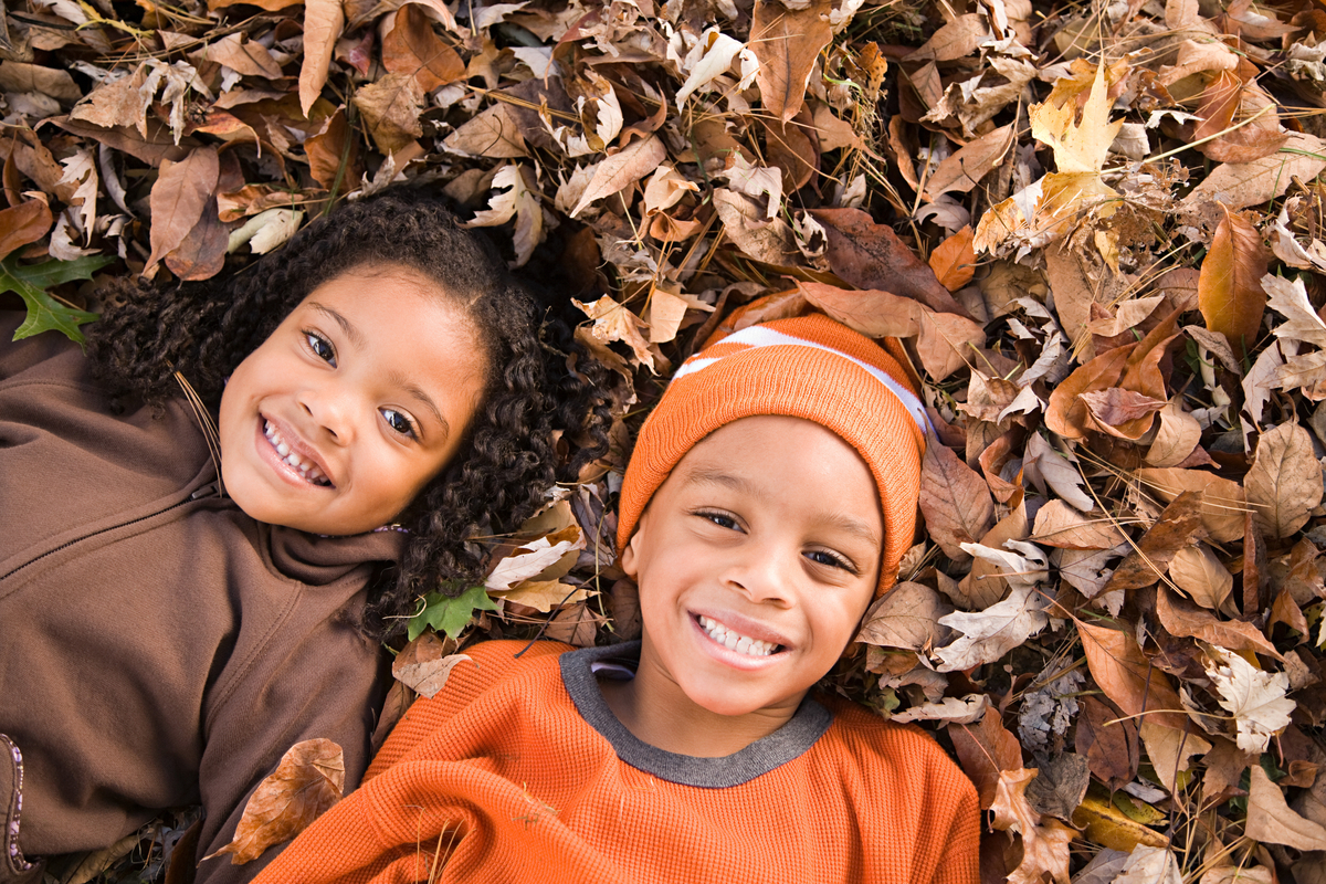 A couple of kids lying in a pile of leaves