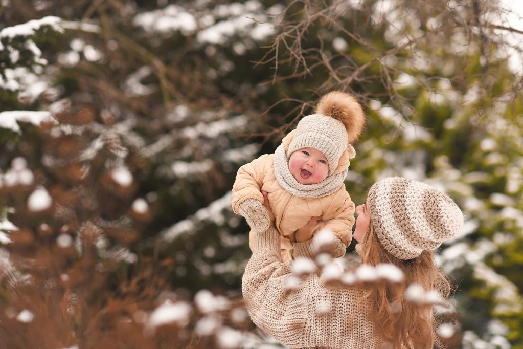 A parent holding up a baby outside in the snow.