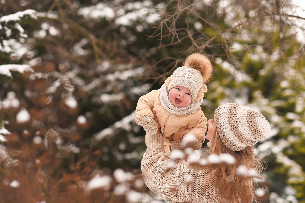 A parent holding up a baby outside in the snow