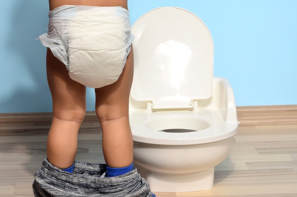 A toddler in a diaper standing in front of a potty