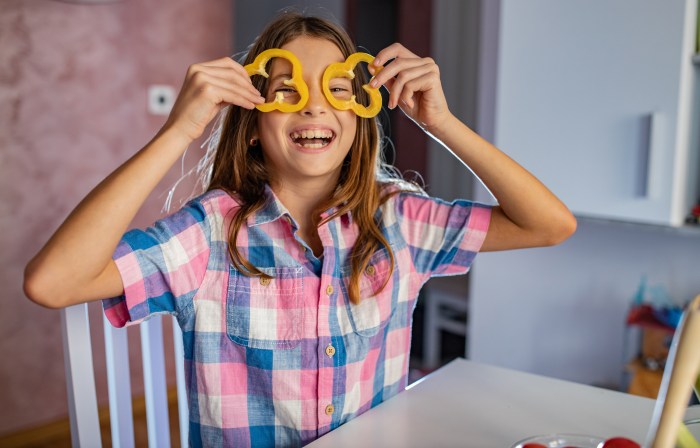 A child is holding slices of peppers up to her eyes.