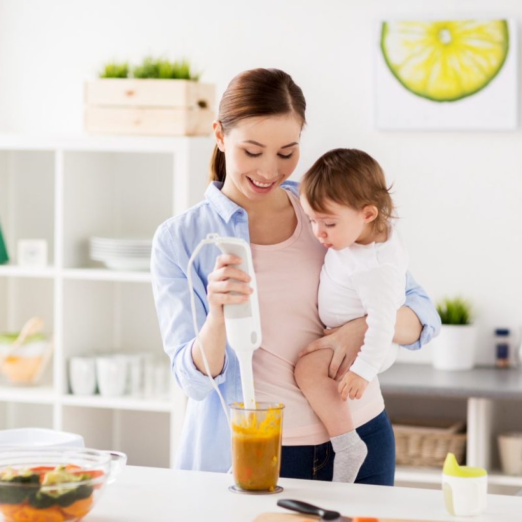 A mother holding her baby while making baby food.