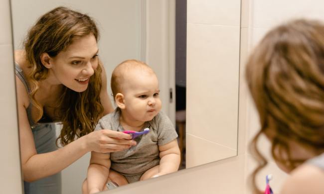 A mom holds the toothbrush for the baby