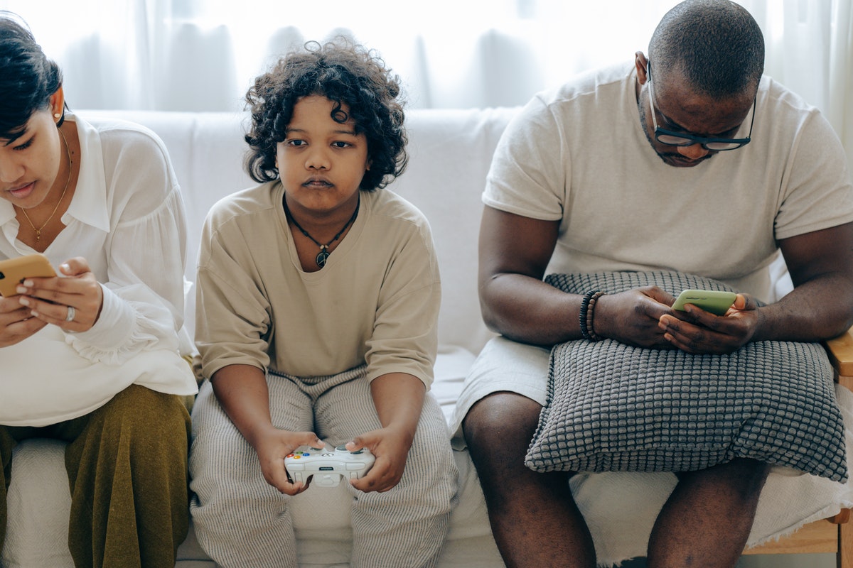 Child playing video game sitting in between parents on phones