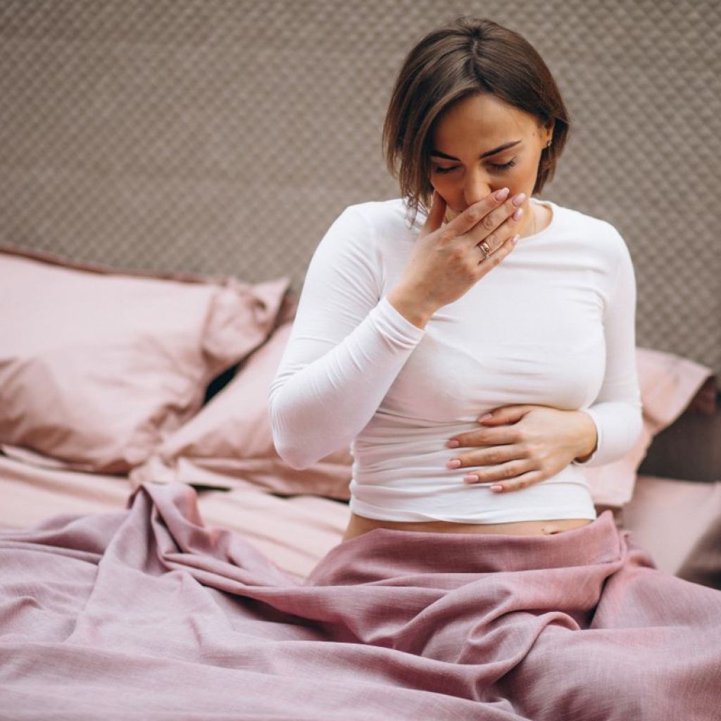 Lady sitting at edge of bed with her hand on her mouth