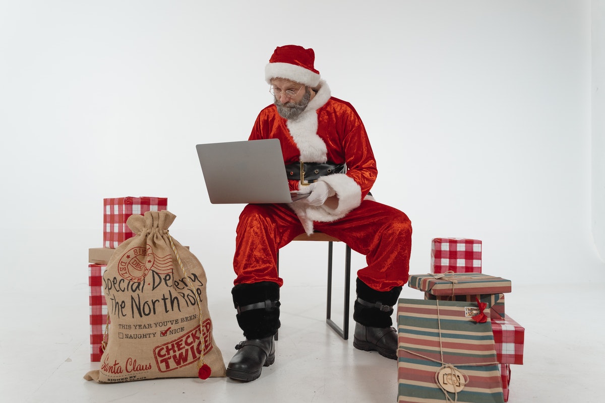 Santa looking at list on a laptop with presents around him.