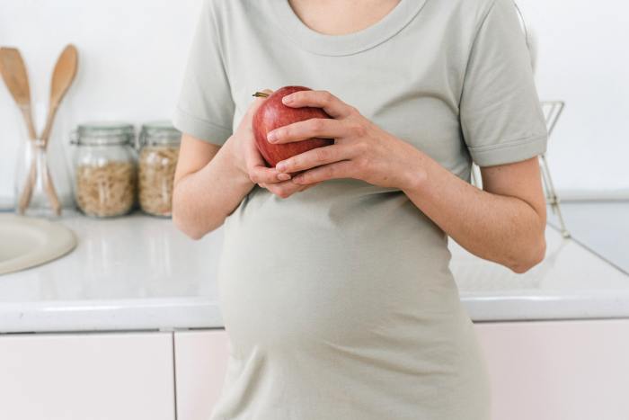 Pregnant person holding an apple.
