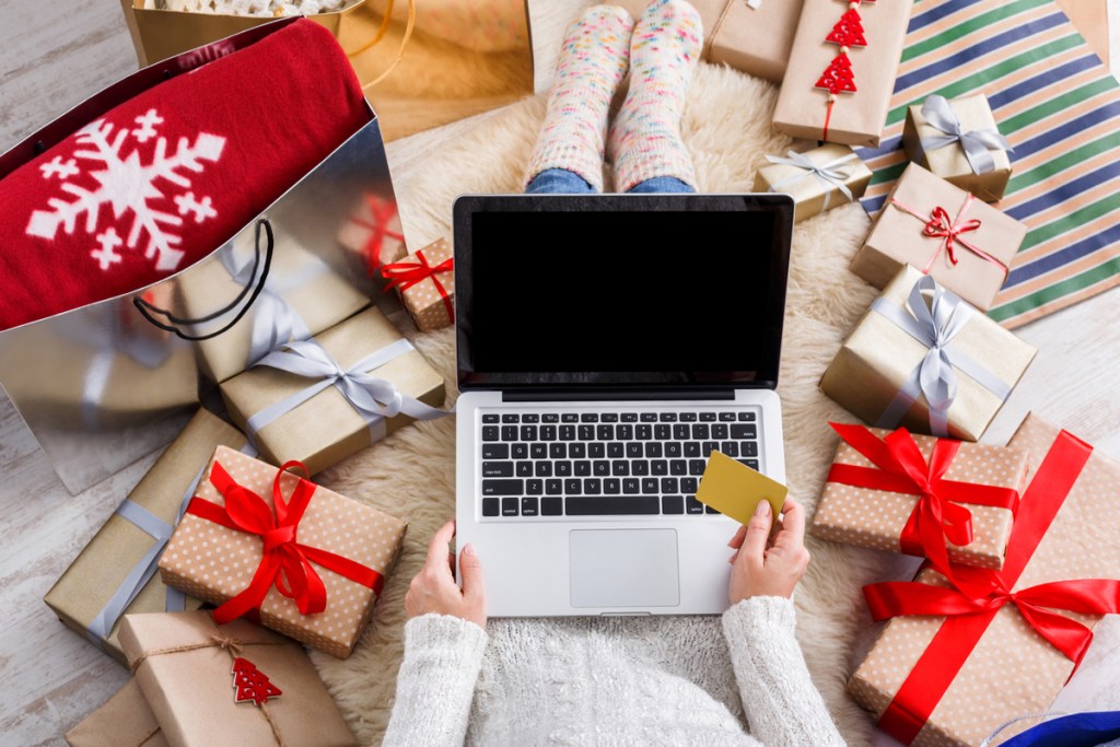 A person doing holiday shopping on their laptop with presents all around them