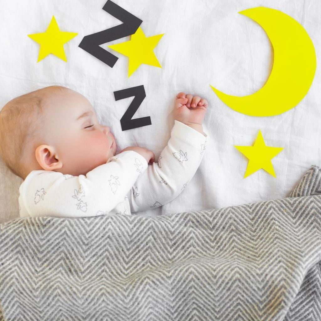 Baby sleeping in crib with a gray blanket and decals