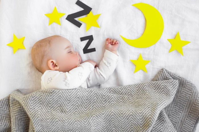 Baby sleeping in crib with a gray blanket and decals