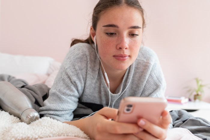 A teenager lies on her bed looking at her phone