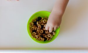 A small child grabbing cereal from a bowl.