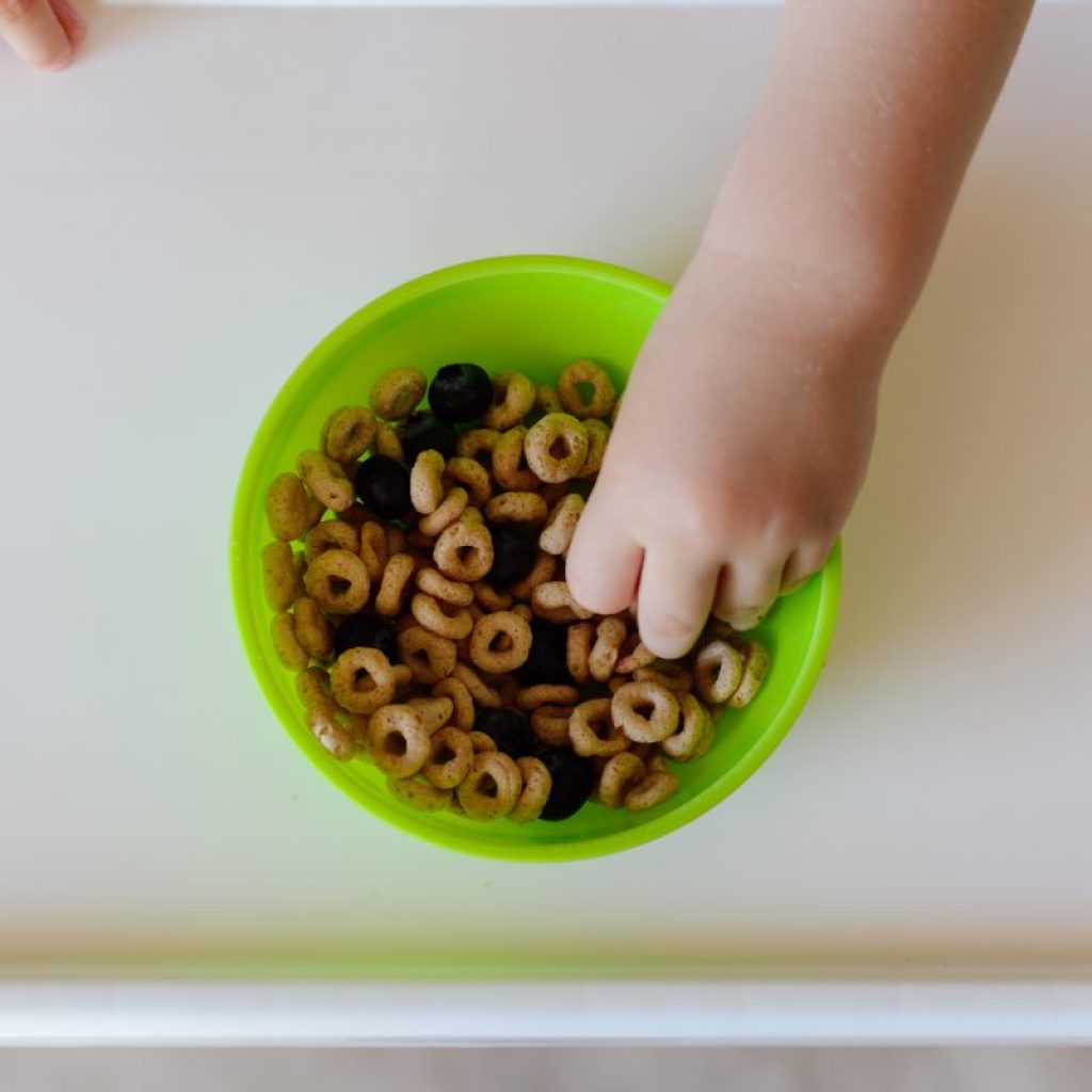 A small child grabbing cereal from a bowl