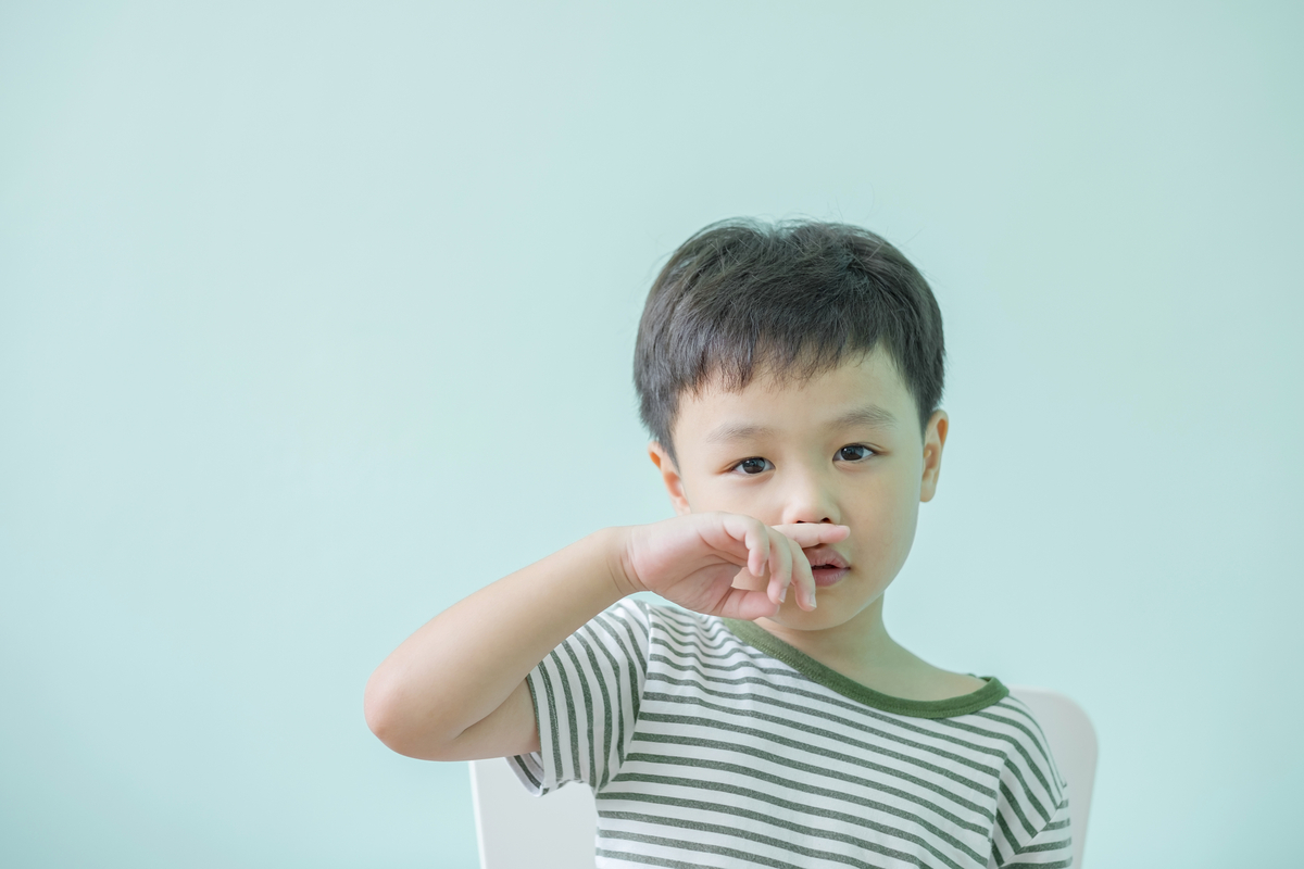 A little boy with his hand by his nose.