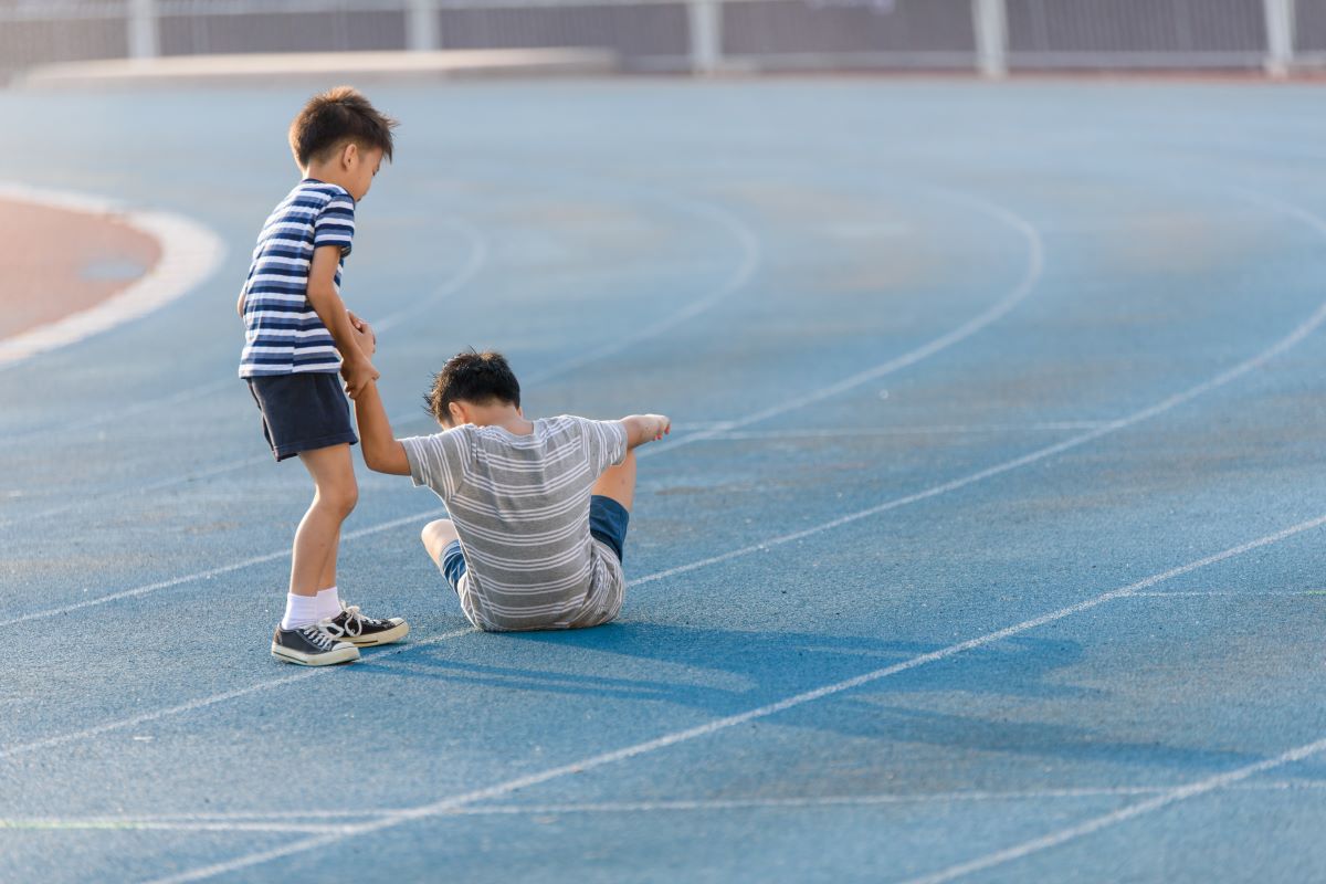 One boy helping another boy to stand up