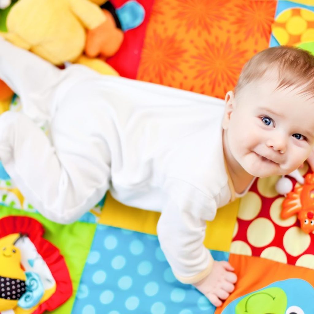 A baby looking up over their shoulder while on a play mat.