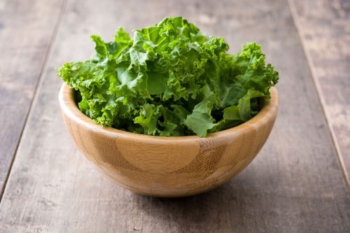 Fresh green superfood kale leaves in wooden bowl on wooden background